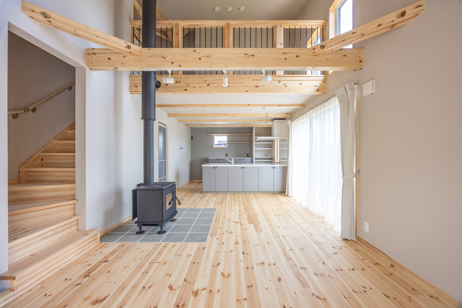 吹き抜けのリビングに設置された薪ストーブが家族の中心に。梁を見せたデザインと無垢の床材が、木の温もりを感じさせます。