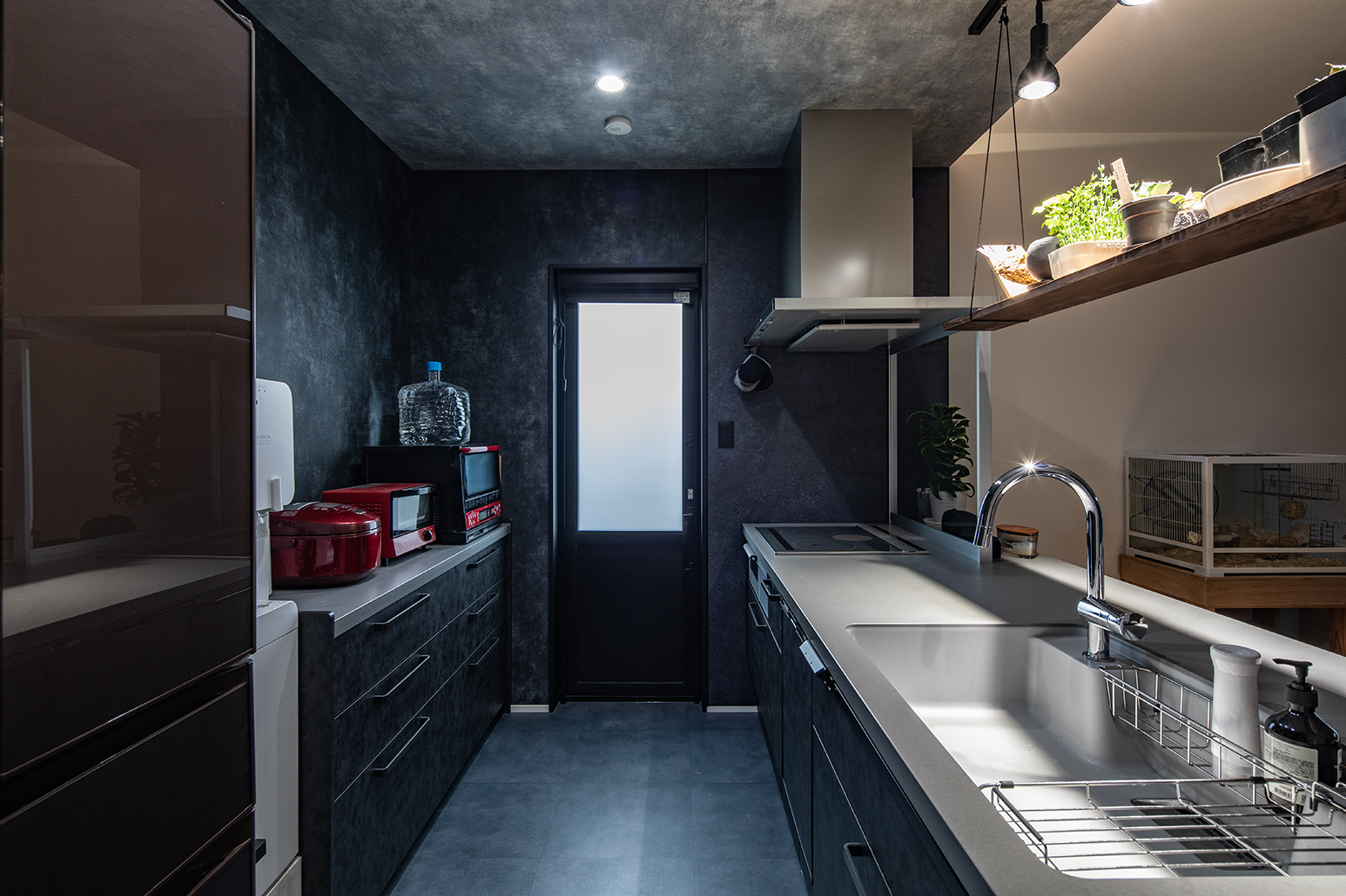 ダクト下に油はね防止のガラスを入れたキッチン。壁は黒、天井はグレーを基調としたクロスにすることで、リビングダイニング側と空間をゆるやかに仕切った。