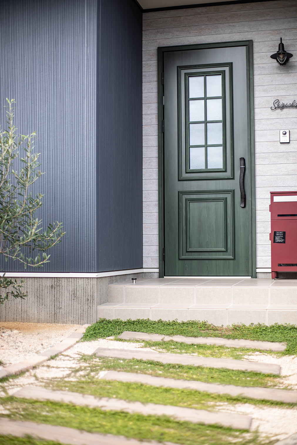 枕木と下草を敷いた緩やかなアプローチの先は、オリーブグリーンのこだわりを玄関ドアが迎えてくれる。