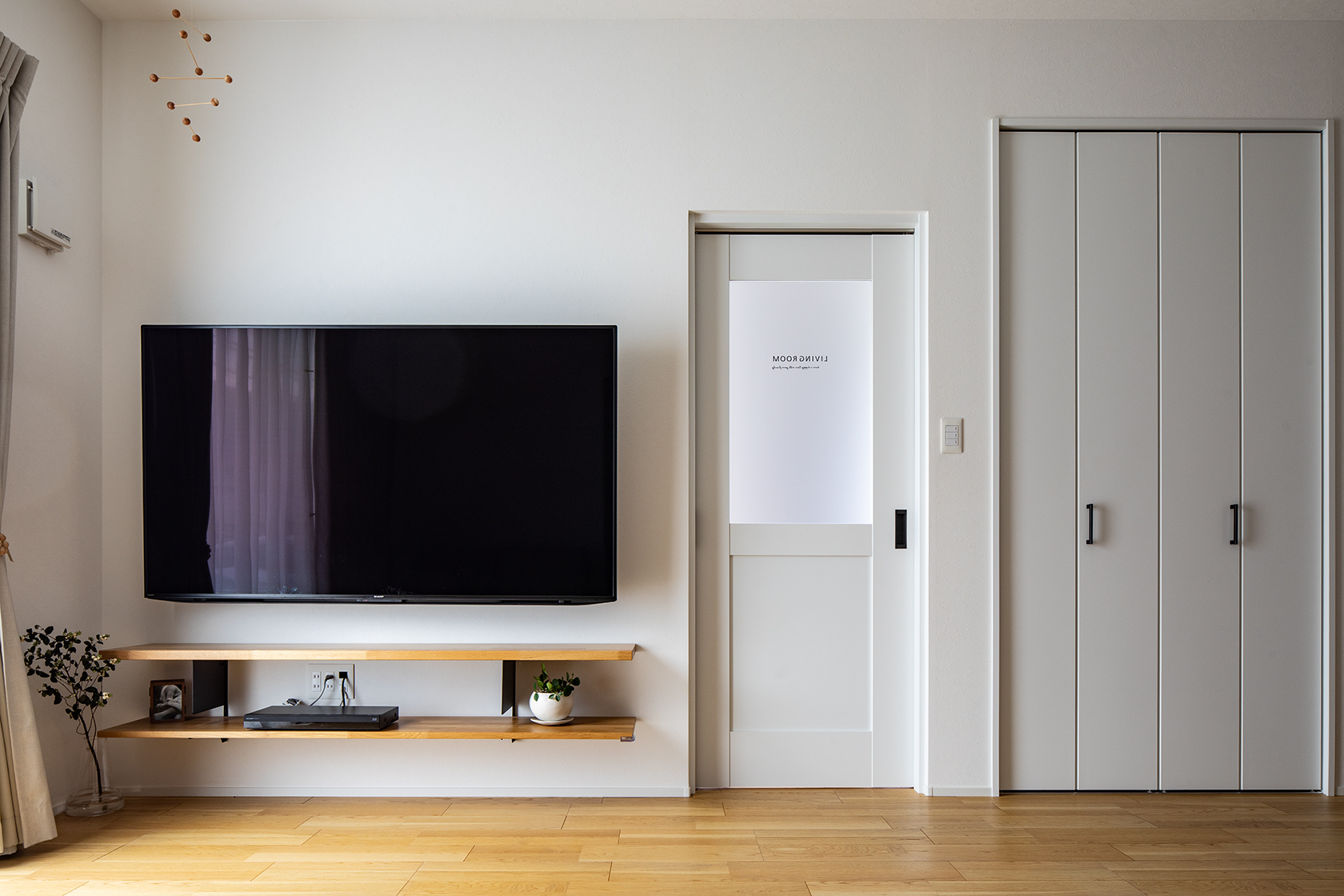 もともとシンプルなデザインが好きなM様ご夫婦。壁や建具は白を基調にすっきりと。テレビ横のドアを開けると玄関ホールにつながる。