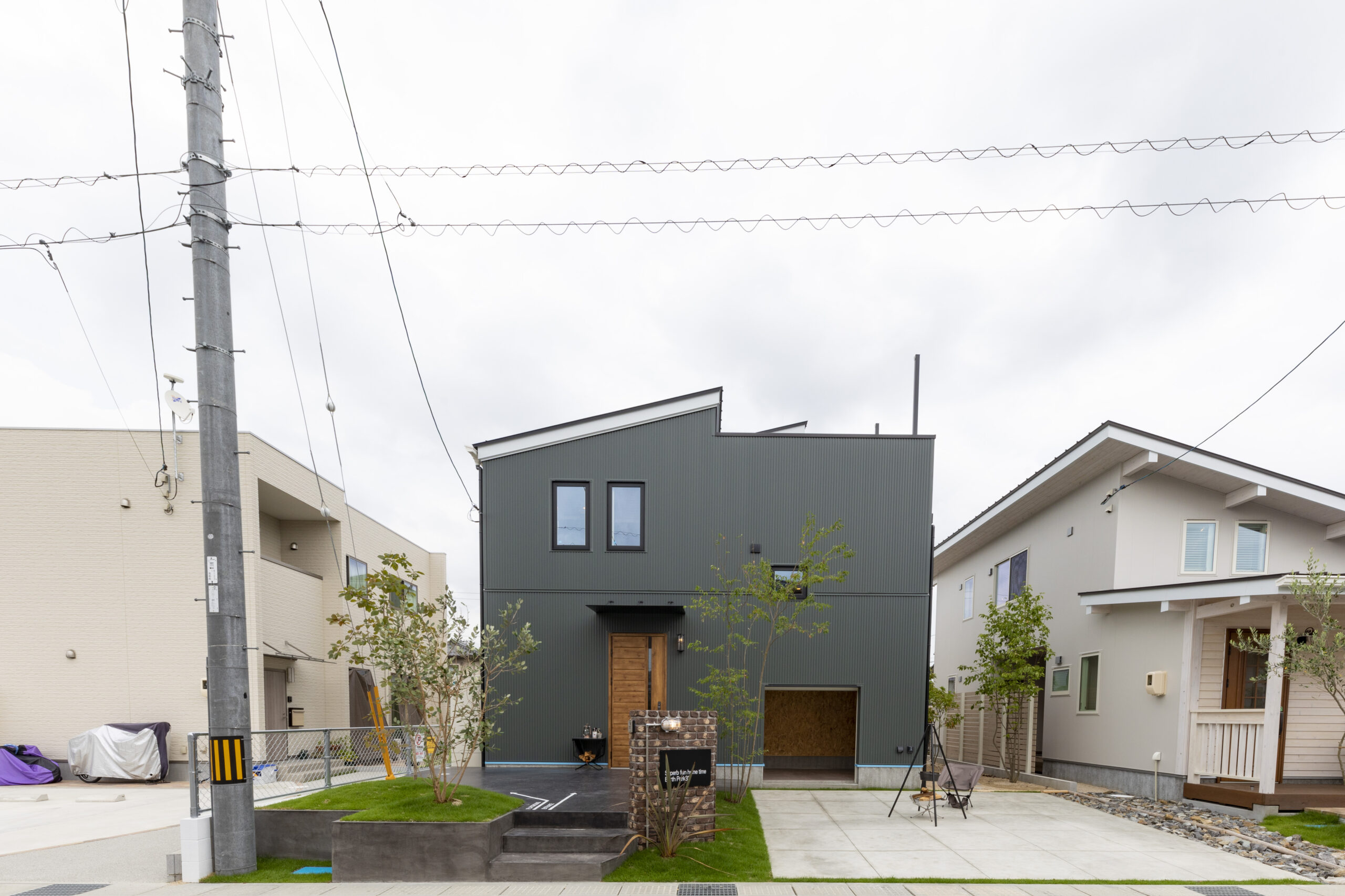 モスグリーンのモダン外観。ガレージと植栽が調和。