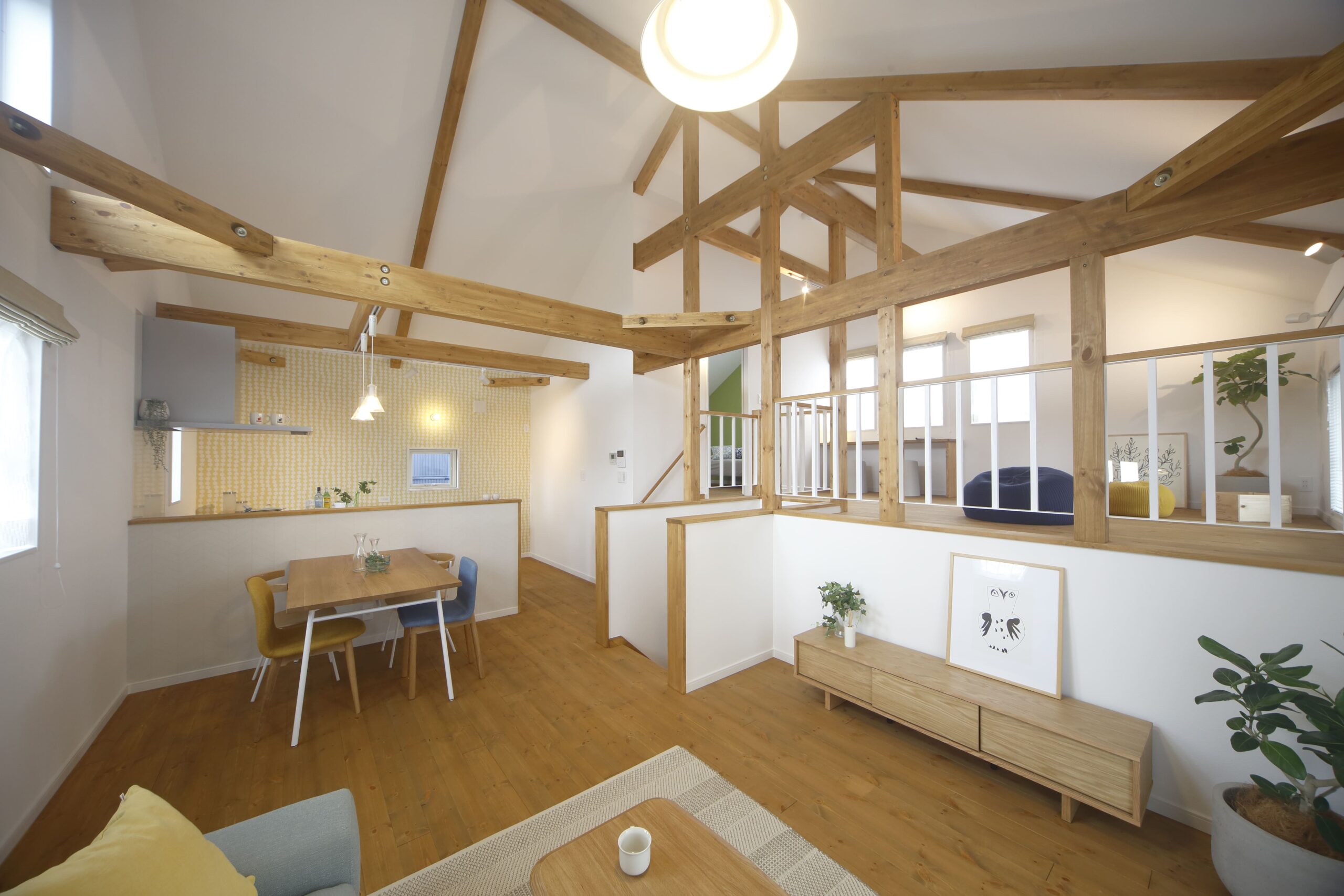 木の梁が印象的な吹き抜け空間と、スキップフロアでつながるダイニング。北欧テイストの明るい配色が、家族の会話を自然と弾ませます。