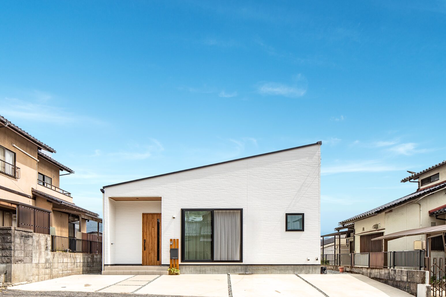白い壁に黒の窓枠、そして木製の玄関ドアのバランスが絶妙で、シャープな片流れの屋根が印象的。4台分の駐車スペースを確保しているので来客があっても安心。