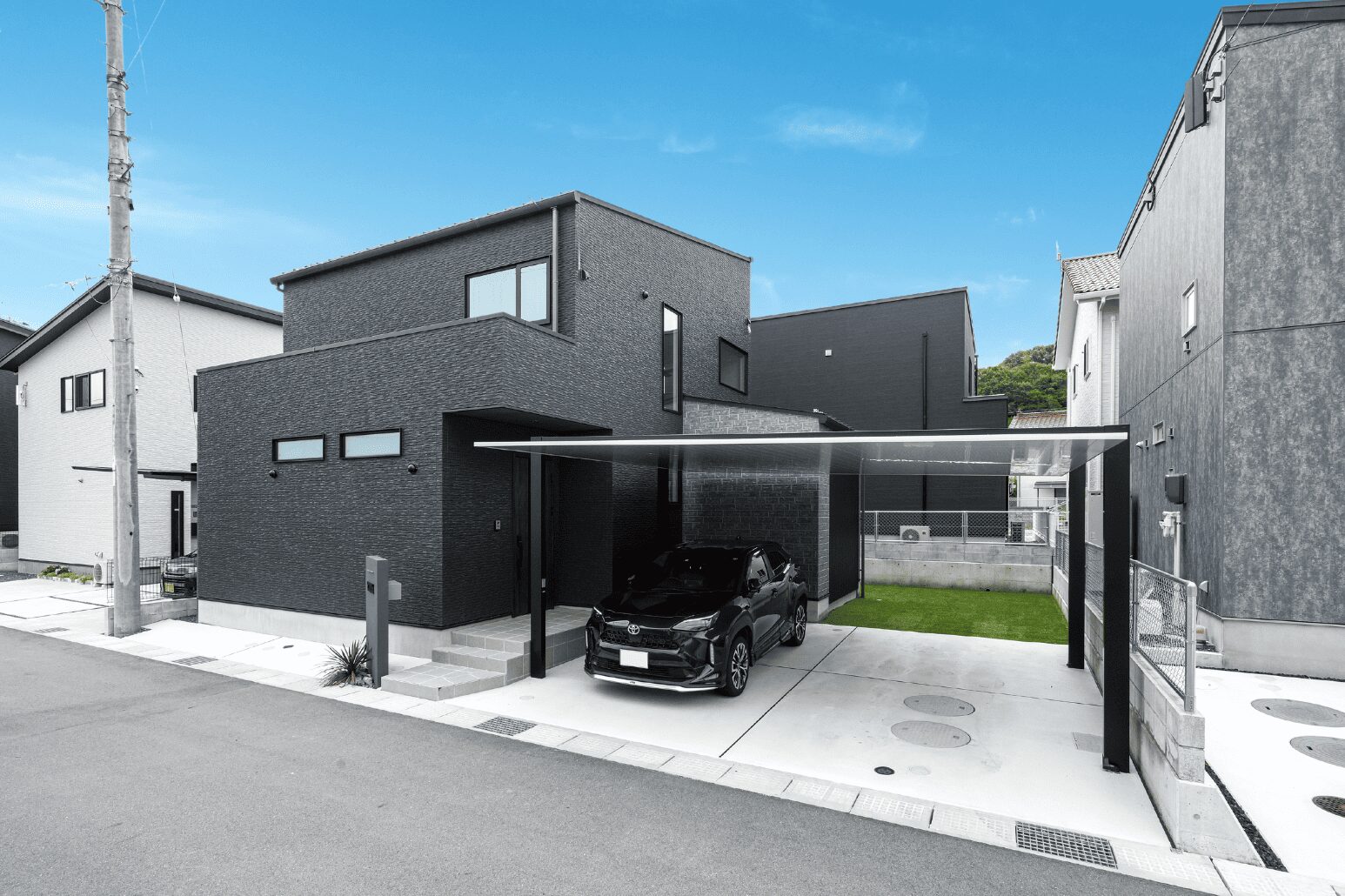 外観は黒基調なシックなトーンで統一。カーポートのシルバーの屋根材がひときわスタイリッシュ。少し角度をつけて設置されたグレーの門柱がアクセントに。