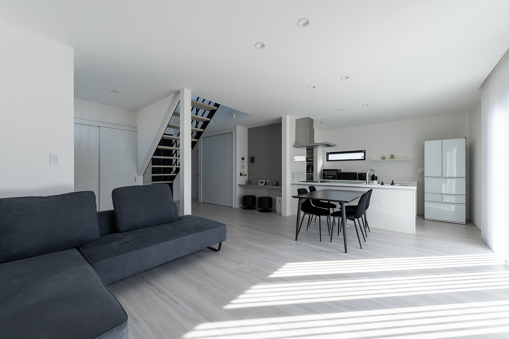 ブラインドから差し込む光とモノトーンのインテリアが美しいLDK。リビング階段にしたことで、家族の帰宅や外出が確認しやすい。