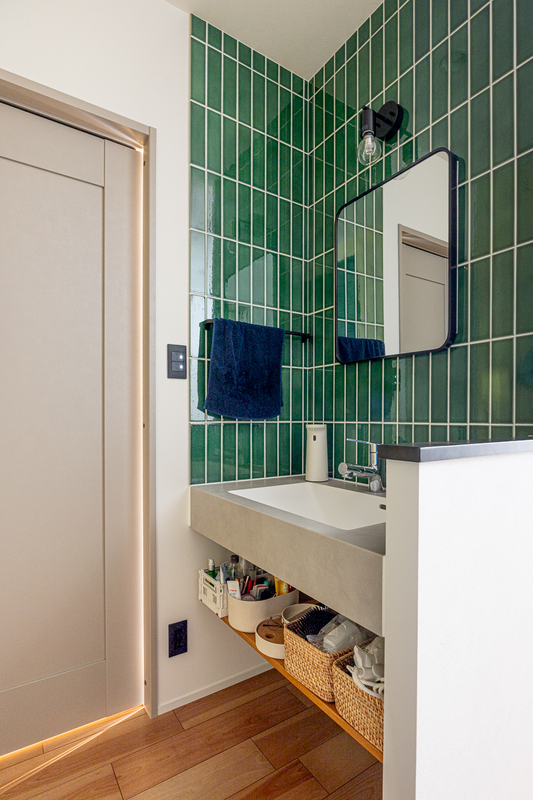 深い緑色の縦型タイルが印象的な洗面スペース。造作洗面台の下部にはオープン収納を設け、機能性とデザイン性を両立している。