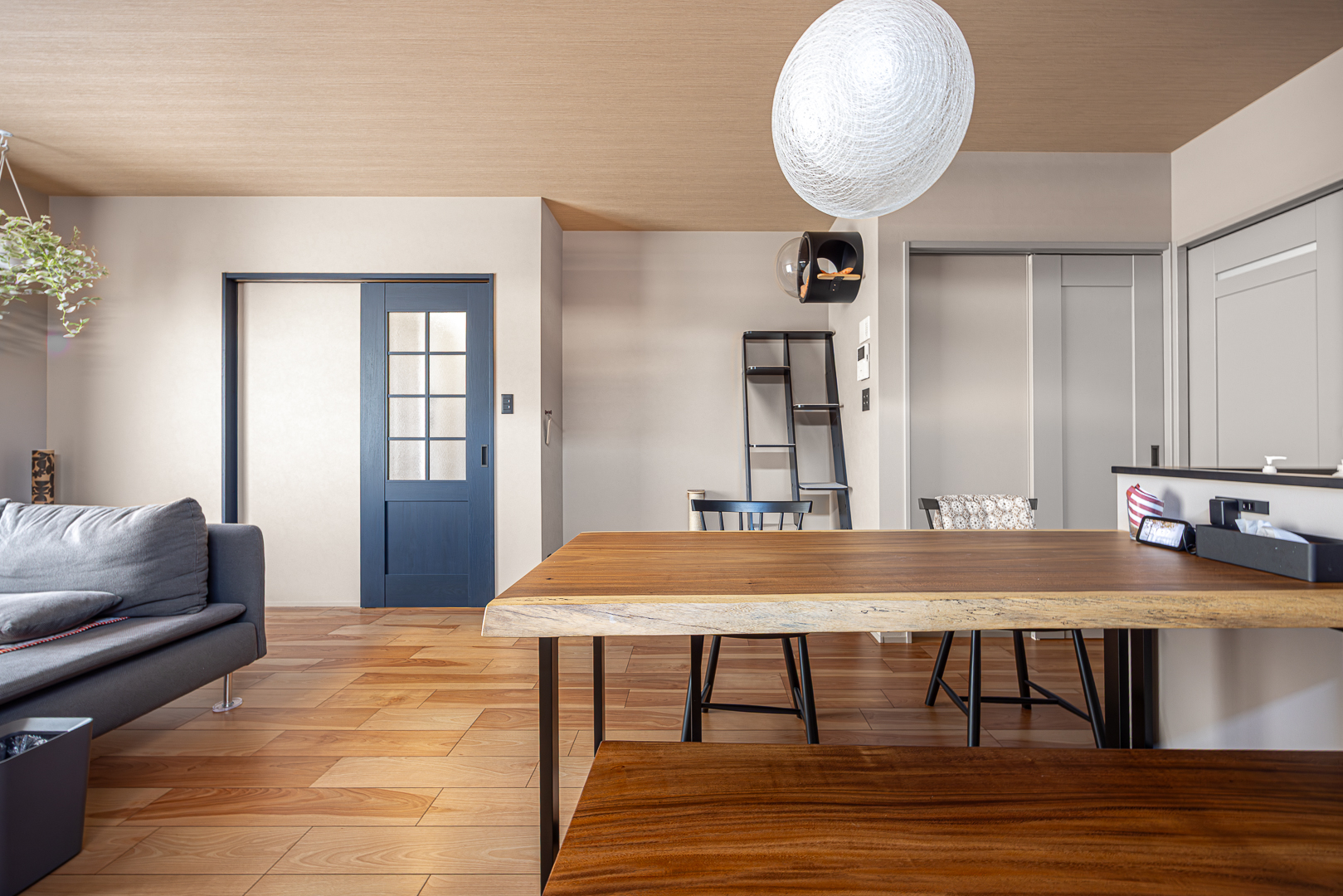 一枚板ダイニングテーブルが存在感を放つLDK。木目天井とフローリングが温かみを添え、グレージュの壁と黒のアクセントがモダンな雰囲気を演出。奥には猫ちゃんコーナーが見える。